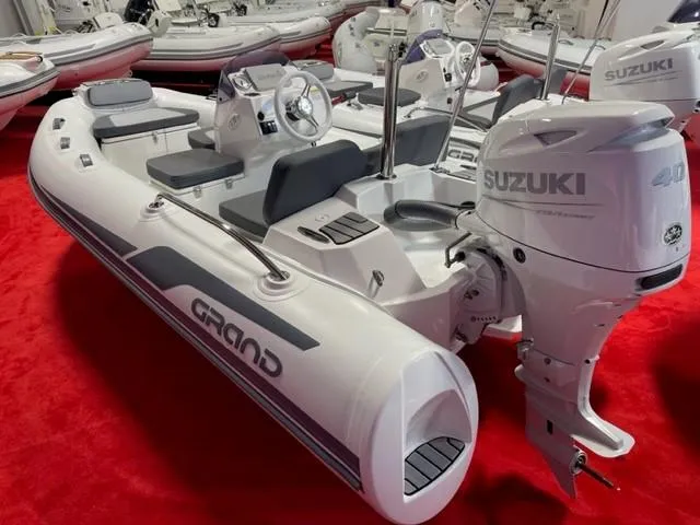 Slide: The Image of 2025 Grand Inflatables G380 boat with Suzuki engine on red carpet display. - 1