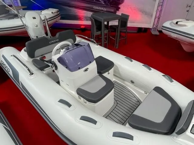 Slide: The Image of 2025 Grand Inflatables G380 boat with sleek design on display, featuring gray seating and red carpet backdrop. - 6