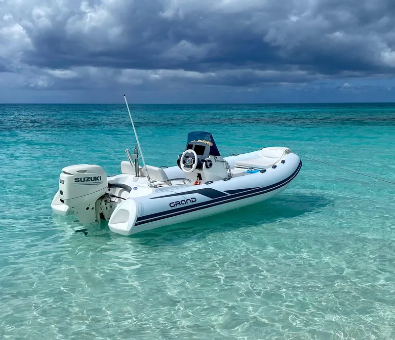Slide: The Image of 2025 Grand Inflatables G420 boat floating on clear turquoise water under cloudy skies. - 1