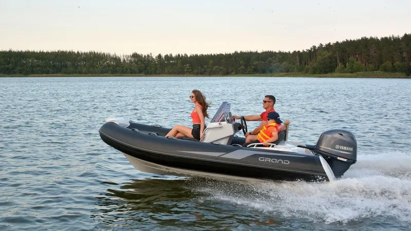 Slide: The Image of 2025 Grand Inflatables G420 boat cruising on a lake with two passengers. - 10