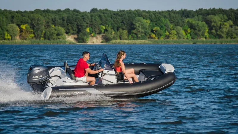 Slide: The Image of 2025 Grand Inflatables G420 boat cruising on a lake with two passengers. - 11