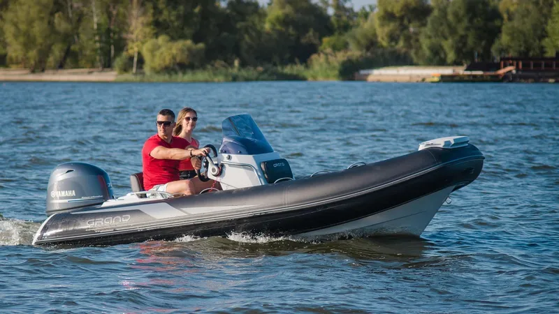 Slide: The Image of 2025 Grand Inflatables G420 boat cruising on a lake with two passengers. - 14