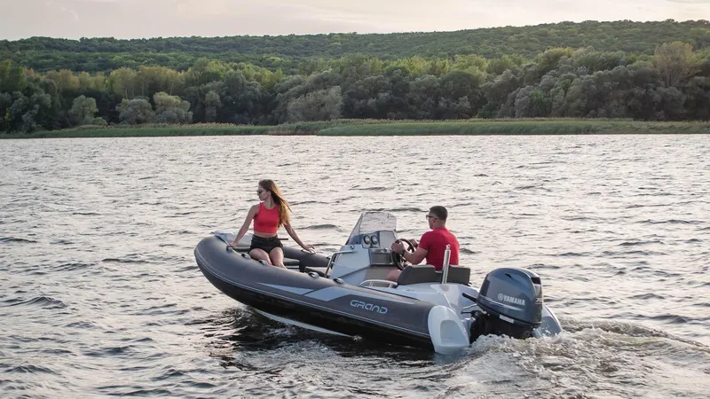 Slide: The Image of 2025 Grand Inflatables G420 boat cruising on a scenic lake with two passengers. - 17