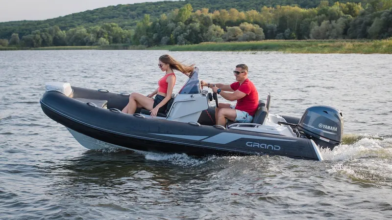 Slide: The Image of 2025 Grand Inflatables G420 boat cruising on a scenic lake with two passengers. - 18