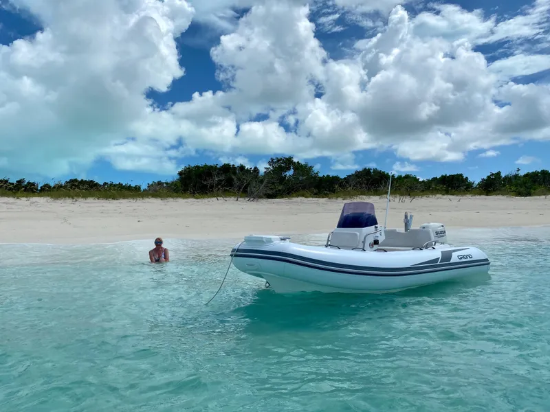 Slide: The Image of 2025 Grand Inflatables G420 boat anchored near a sandy beach under a cloudy sky. - 2