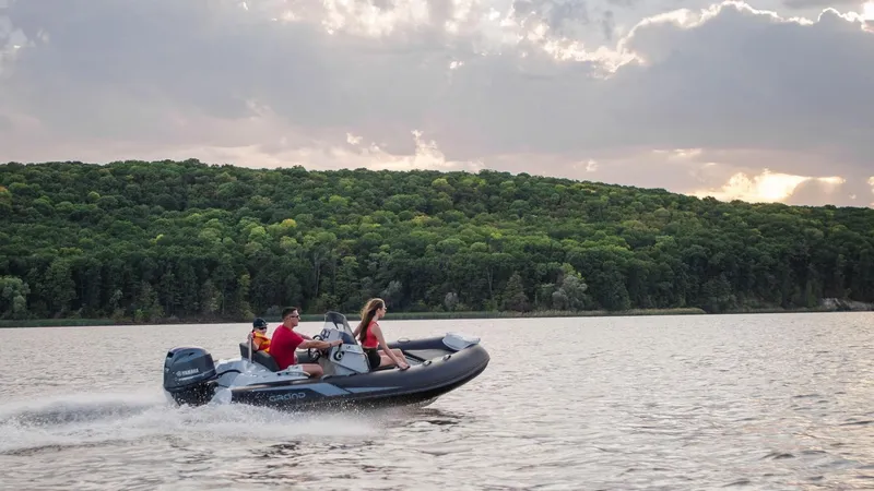 Slide: The Image of 2025 Grand Inflatables G420 boat cruising on a scenic lake with lush green hills. - 22