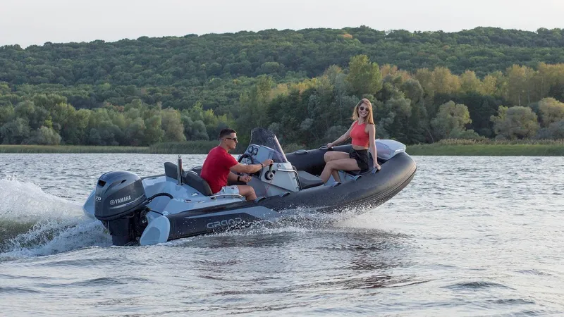 Slide: The Image of 2025 Grand Inflatables G420 boat cruising on a scenic lake with two passengers. - 25