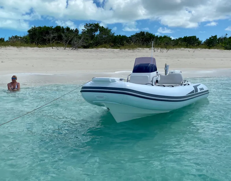 Slide: The Image of 2025 Grand Inflatables G420 boat anchored near a sandy beach with clear blue water. - 3