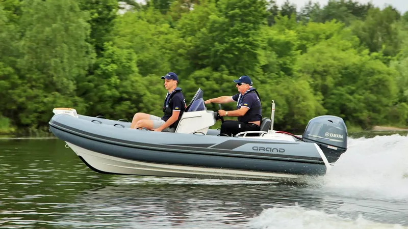 Slide: The Image of 2025 Grand Inflatables G420 boat cruising on a lake with two passengers. - 9