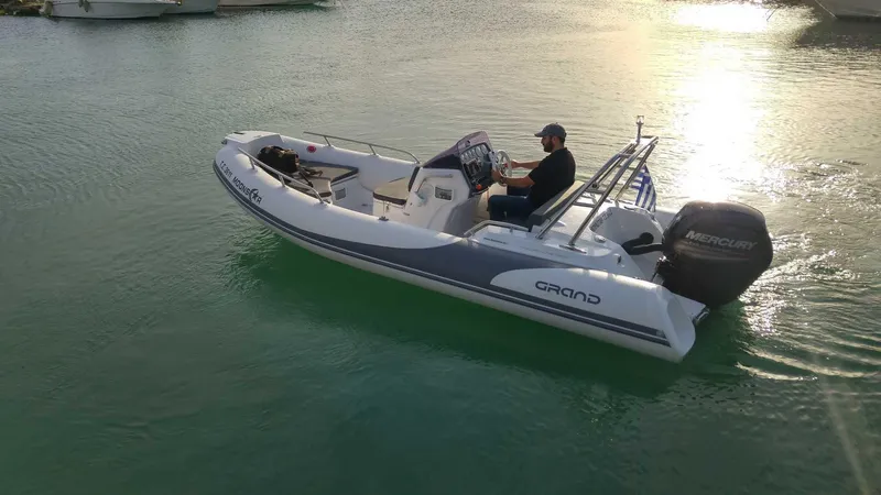 Slide: The Image of 2025 Grand Inflatables G500 boat on water, featuring a Mercury engine, with a person steering. - 2