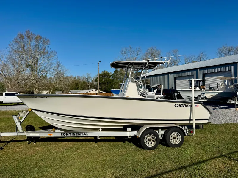 Slide: The Image of 2008 Contender 21 Open boat on trailer, parked on grass near a metal building. - 2