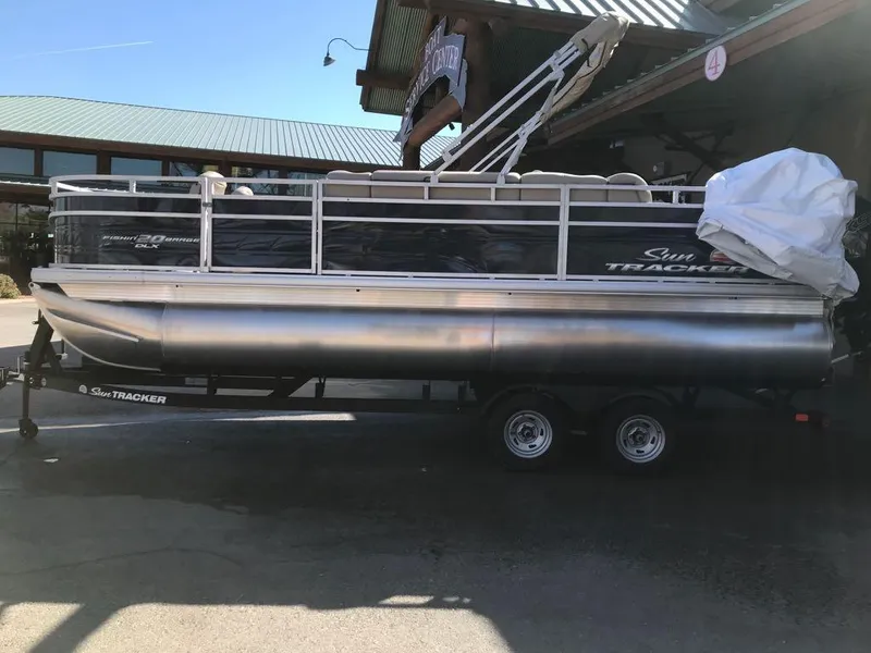 Slide: The Image of 2025 Sun Tracker Fishin' Barge 20 DLX pontoon boat on trailer, parked outdoors. - 2