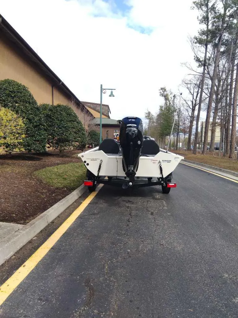 Slide: The Image of 2025 Tracker Pro Team 175 boat on trailer, parked on a road near trees and buildings. - 2