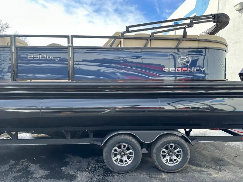 Slide: The Image of 2025 Regency 230 DL3 pontoon boat on trailer, side view, blue and black design. - 4