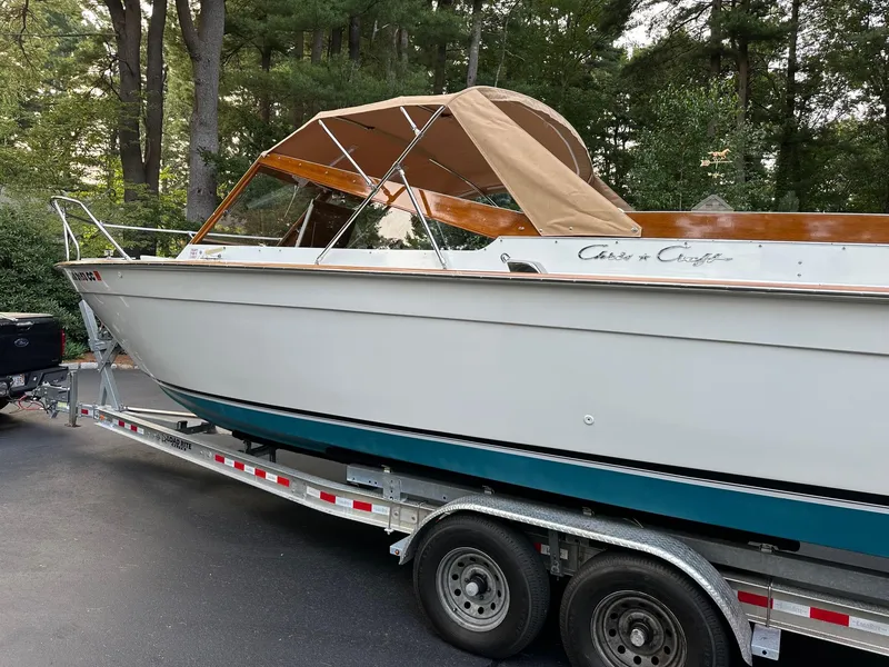 Slide: The Image of 1973 Chris-Craft Sport Deck boat on trailer, parked in wooded area. - 2