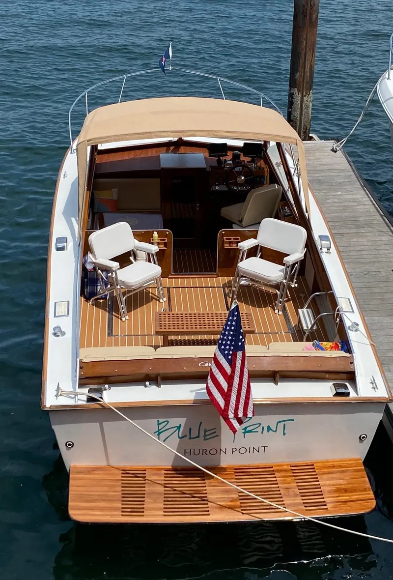 Slide: The Image of 1973 Chris-Craft Sport Deck boat docked, featuring wooden deck and American flag. - 3