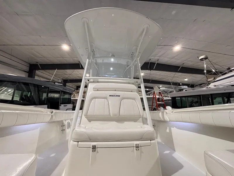 Slide: The Image of 2015 Regulator 25 boat interior with white seating and T-top in a showroom. - 21