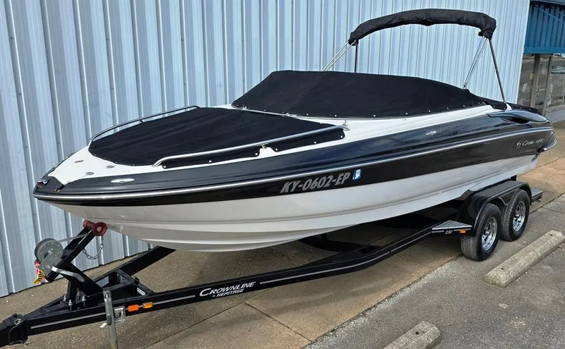 Slide: The Image of 2011 Crownline 230LS BR boat on trailer, black and white design, parked by a metal building. - 18