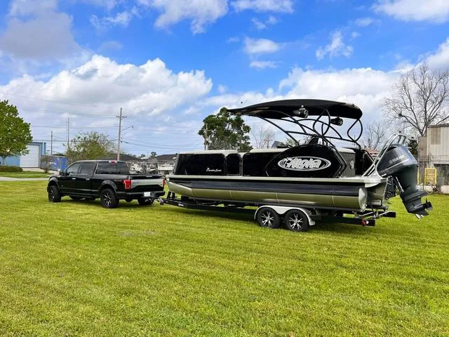 Slide: The Image of 2025 Aloha 23' Paradise Arch Sport Tower boat on trailer, parked on grass under blue sky. - 30
