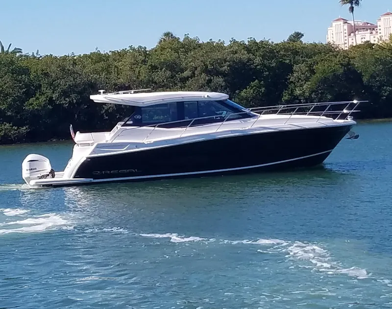 The Image of 2021 Regal 38 XO boat cruising on a sunny day, surrounded by lush greenery. - 0