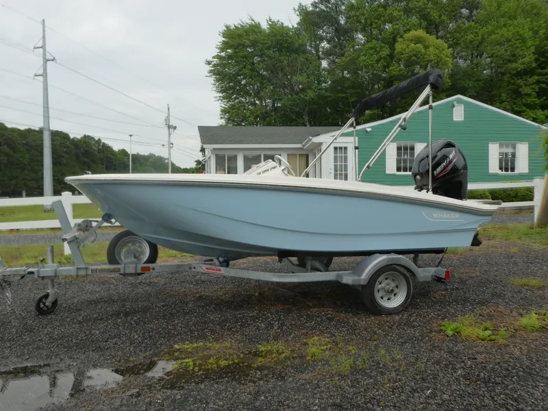 The Image of 2025 Boston Whaler 130 Super Sport boat on trailer, parked outdoors near a green house. - 0