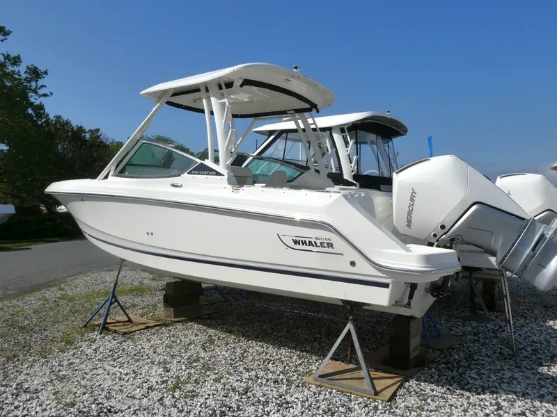 Slide: The Image of 2025 Boston Whaler 240 Vantage boat on display, elevated on stands, with dual outboard engines. - 2