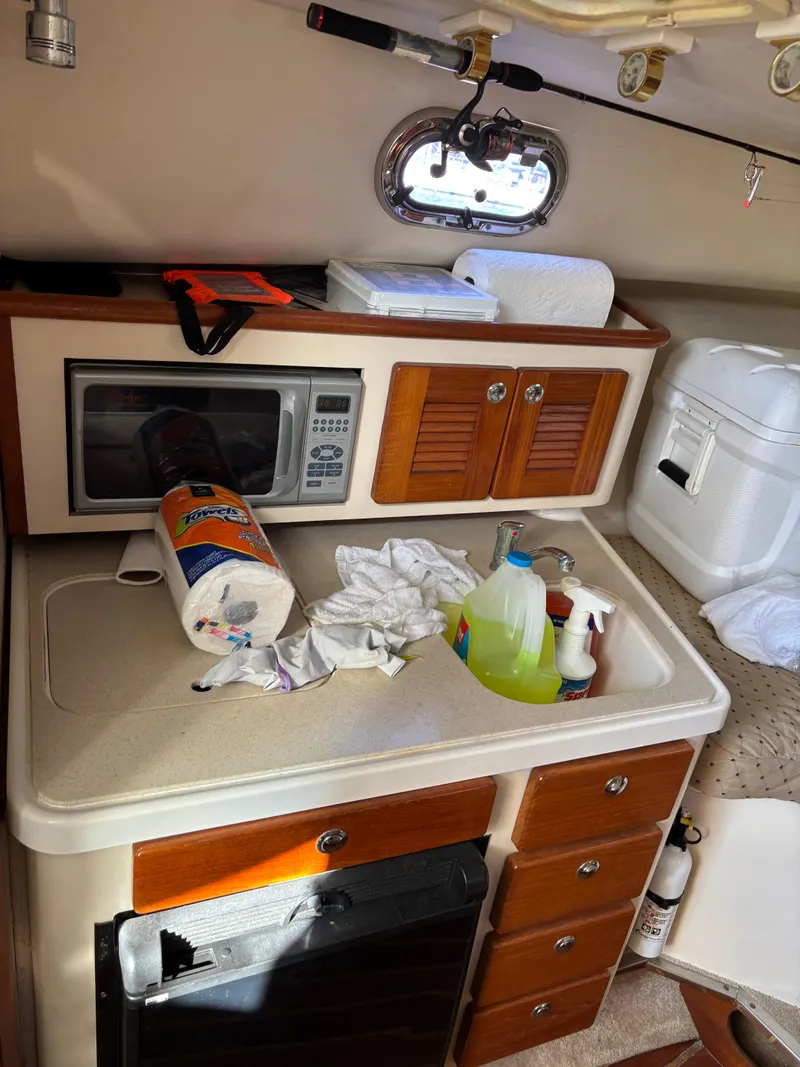 Slide: The Image of 2006 Pursuit 3370 Offshore cabin kitchen with microwave, cleaning supplies, and storage cabinets. - 9