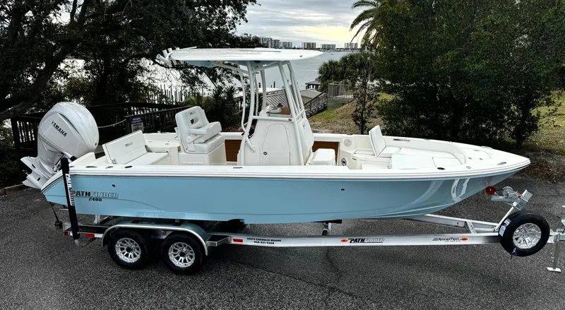 The Image of 2025 Pathfinder 2400TRS boat on trailer, parked outdoors near trees and water. - 0