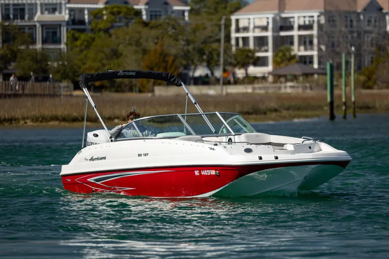 The Image of 2023 Hurricane SunDeck 187 OB boat cruising on water near residential buildings. - 1