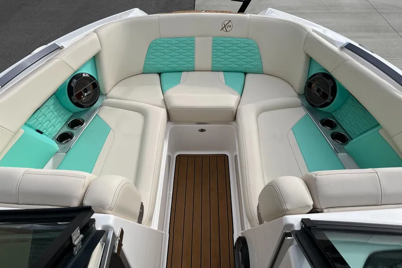 Slide: The Image of 2022 MasterCraft X24 boat interior with teal and white seating, wood flooring, and built-in speakers. - 12