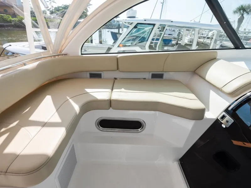 Slide: The Image of 2018 Pursuit OS 385 Offshore boat interior with beige seating and window view. - 34