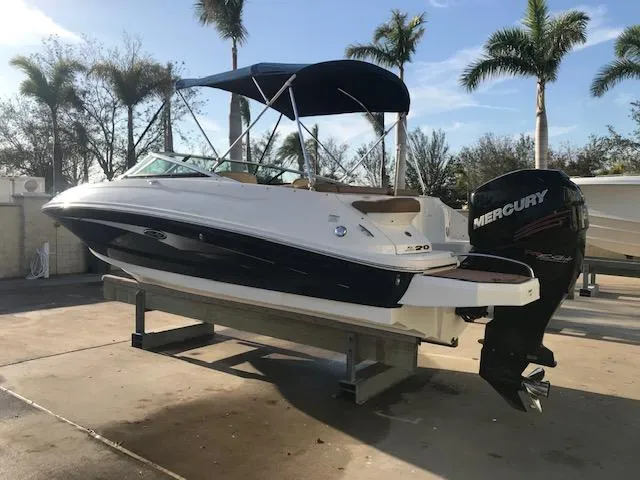 Slide: The Image of 2015 Sea Ray 220 Sundeck Outboard boat on a lift, with palm trees in the background. - 10