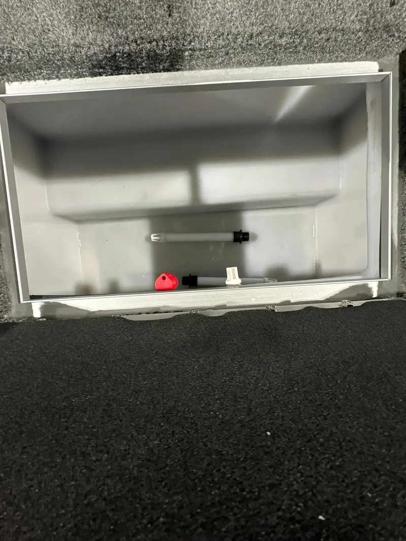 Slide: The Image of 2025 Smoker Craft Adventurer 188 DC storage compartment, empty with a few small items inside. - 3