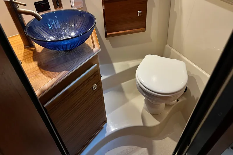 Slide: The Image of 2020 Ranger Tugs 27 bathroom with blue glass sink and wooden cabinetry. - 16