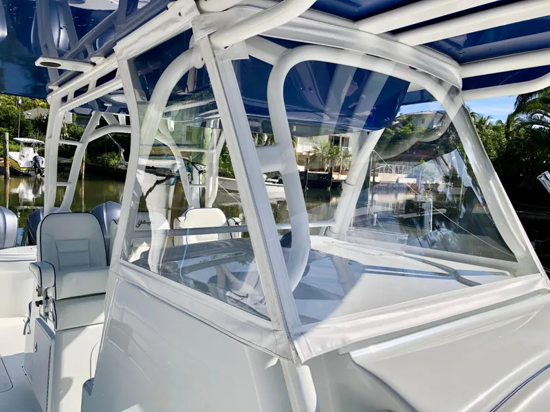 Slide: The Image of 2017 Yellowfin 39 Offshore boat with clear enclosure and blue canopy, docked near lush greenery. - 19
