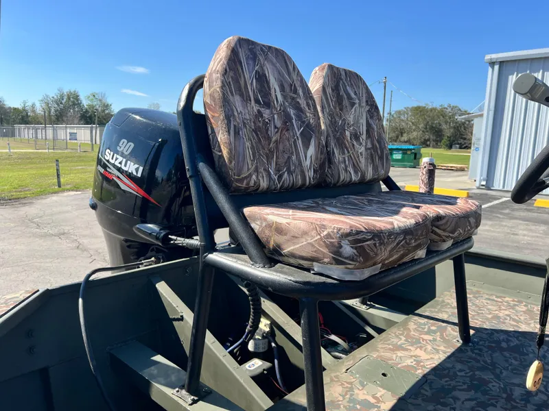 Slide: The Image of 2012 SeaArk 1872 boat with Suzuki 90 engine and camo seats, parked outdoors. - 16