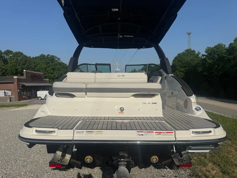 Slide: The Image of 2025 Sea Ray SLX 260 boat, rear view, parked on gravel, with trees and building in background. - 4