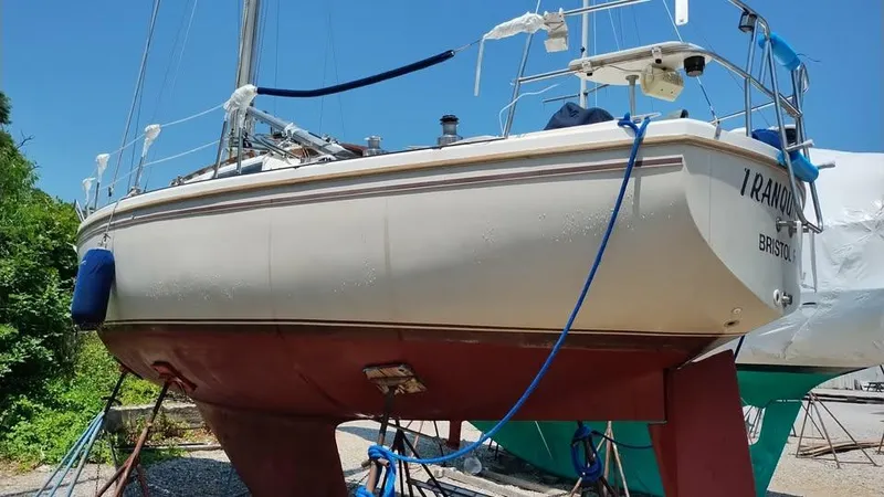 Slide: The Image of 1984 Catalina Sloop sailboat on land, blue sky background, secured with ropes. - 2