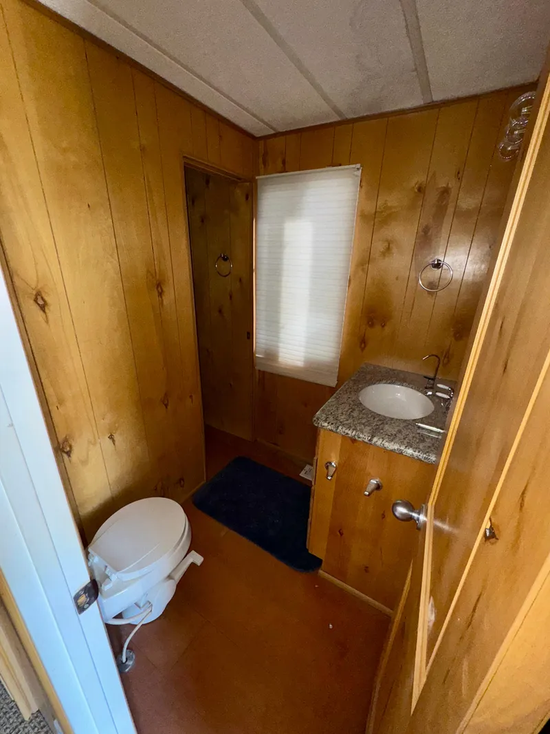 Slide: The Image of Small wooden bathroom with toilet, sink, and window in a 1993 Lakeview Full Ownership model. - 9