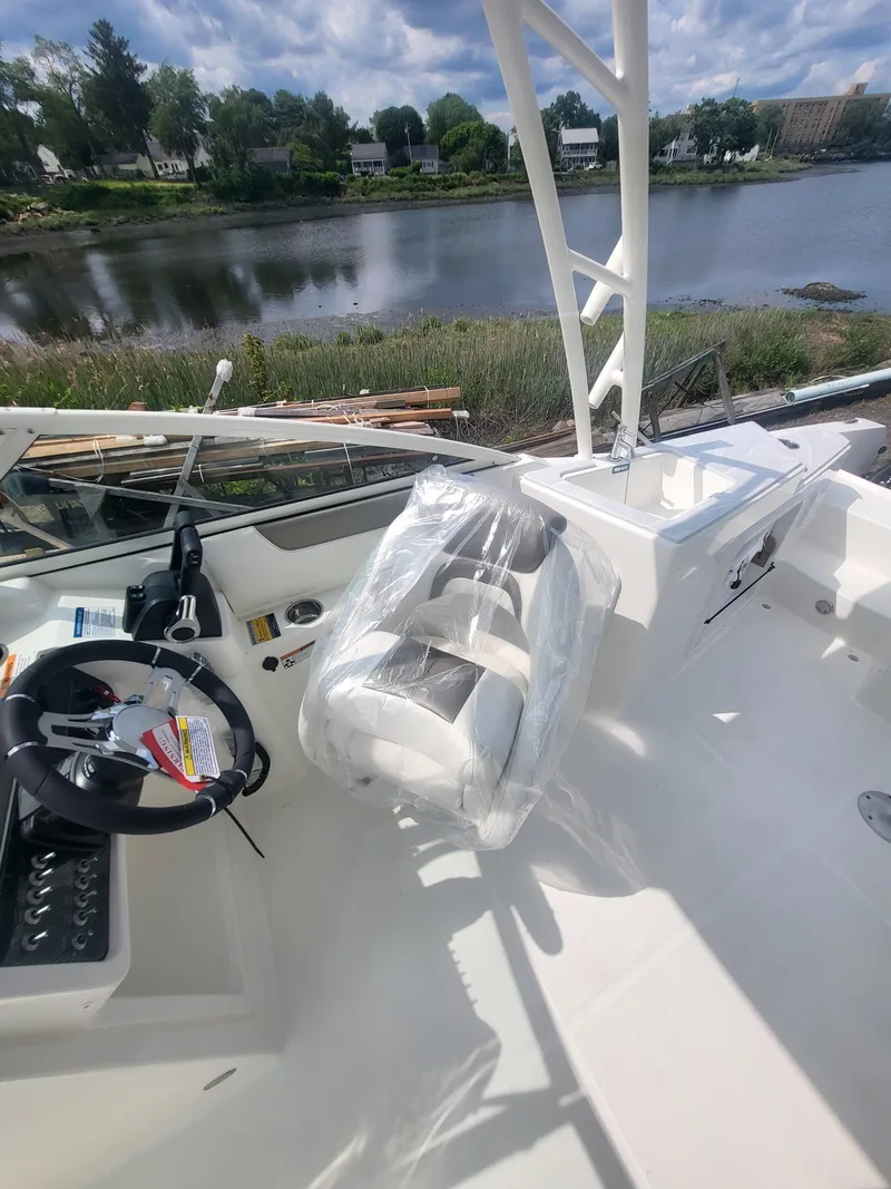 Slide: The Image of 2024 World Cat 230 SD boat interior with steering wheel and seating, near a scenic waterfront. - 5