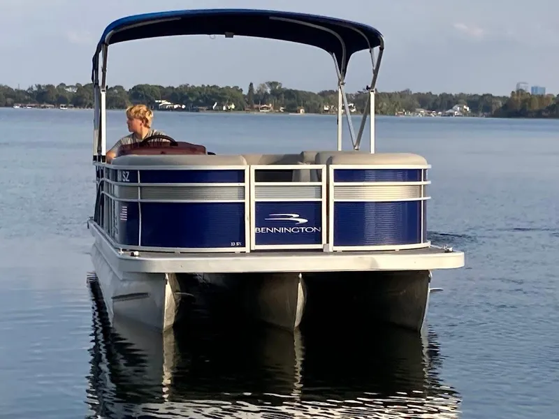 Slide: The Image of 2021 Bennington SX23 pontoon boat on a calm lake, featuring a 175HP Mercury engine. - 2