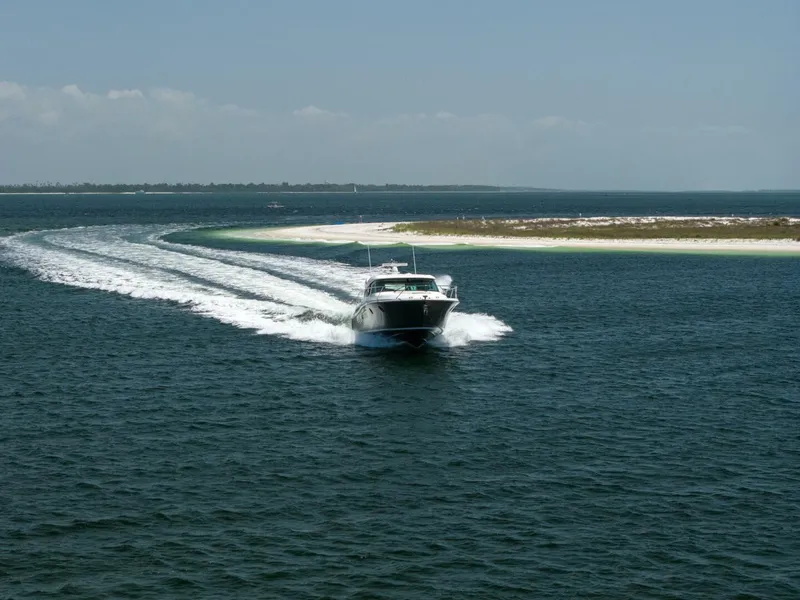 Slide: The Image of 2015 Tiara Yachts 44 Coupe cruising on open water near a sandy shoreline. - 29