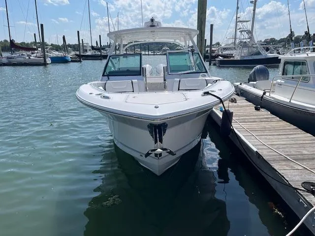 Slide: The Image of 2024 Blackfin 302 DC boat interior with seating and helm, docked by rocky shoreline. - 8