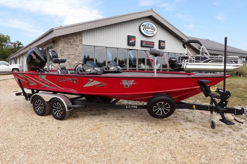 The Image of 2025 Lund 2075 Pro-V Bass XS boat in red, parked outside a marine center. - 2