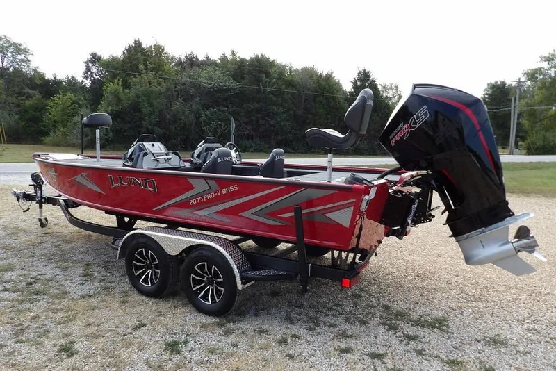 Slide: The Image of 2025 Lund 2075 Pro-V Bass XS boat, red, on a trailer, parked outdoors. - 4