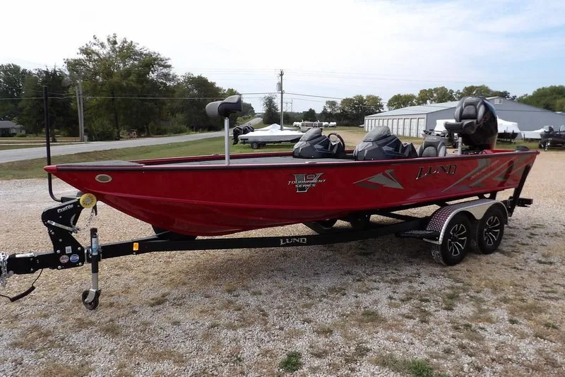 Slide: The Image of 2025 Lund 2075 Pro-V Bass XS boat in red on a trailer, parked outdoors. - 6