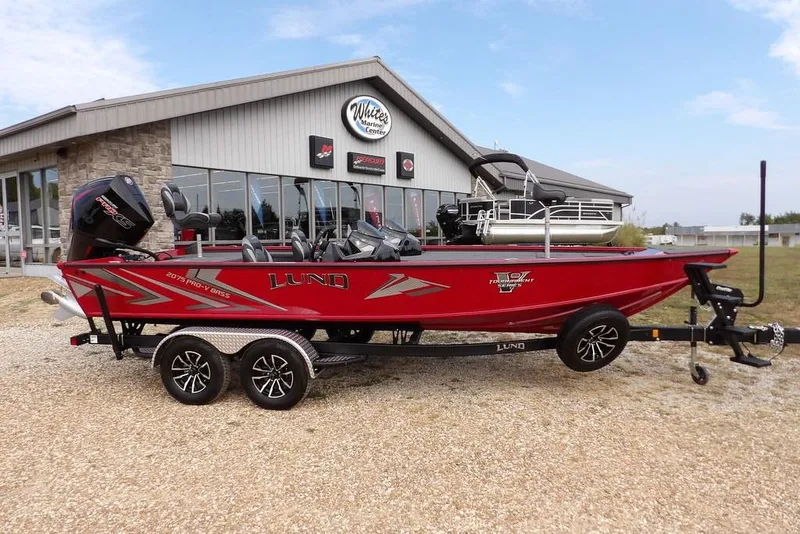Slide: The Image of 2025 Lund 2075 Pro-V Bass XS boat in vibrant red, parked outside a marine center. - 7