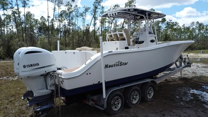 Slide: The Image of 2019 NauticStar 28 XS Offshore boat on trailer with Yamaha engine in wooded area. - 17