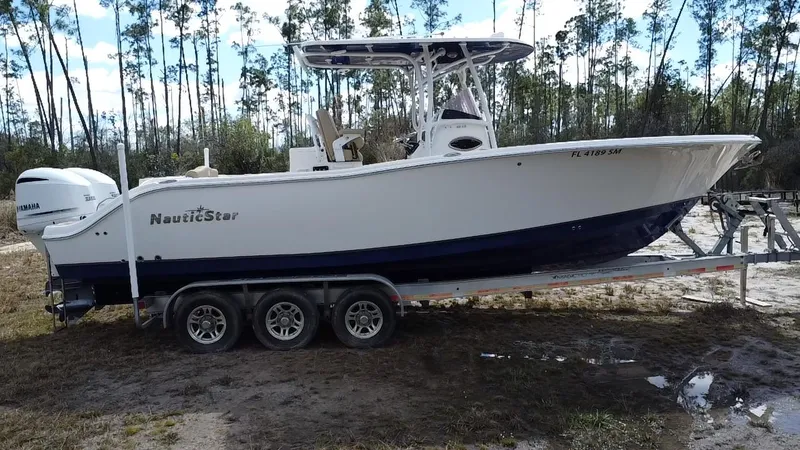 Slide: The Image of 2019 NauticStar 28 XS Offshore boat on trailer in wooded area. - 18