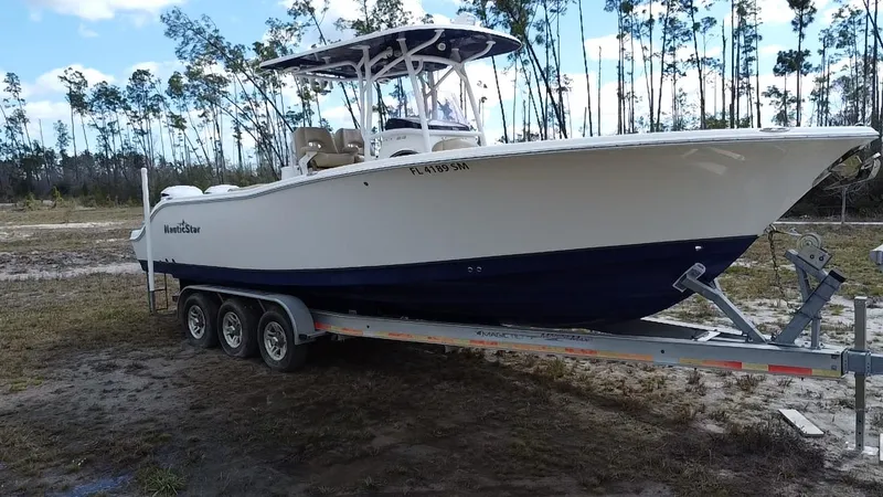 Slide: The Image of 2019 NauticStar 28 XS Offshore boat on trailer, parked outdoors with trees in background. - 19